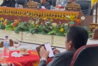 Sekda Tanggamus, Suaidi tertangkap kamera memainkan handphone saat rapat paripurna DPRD, Jumat (08/08/2025). (foto: ist)